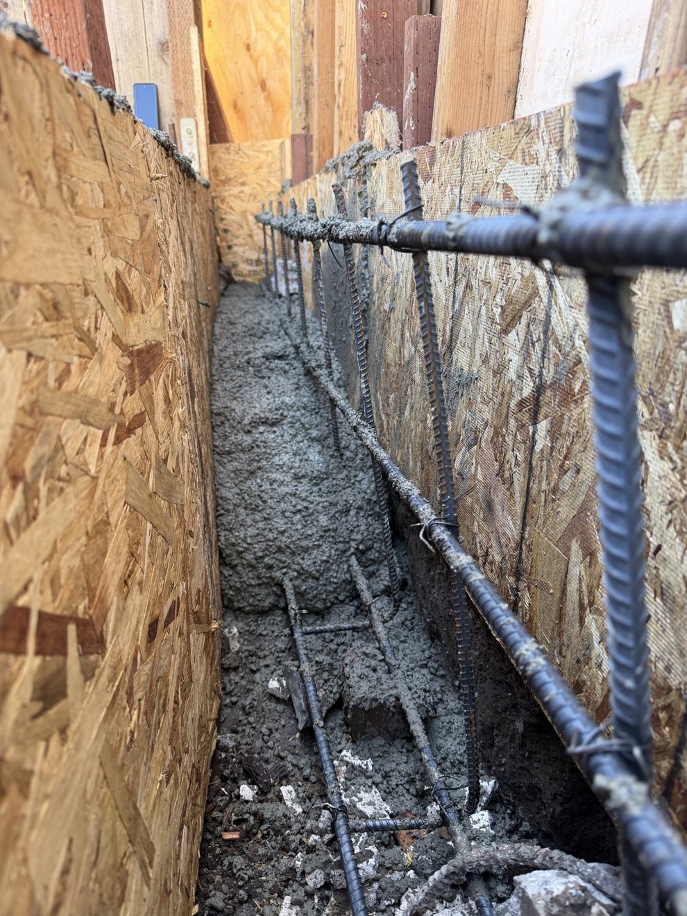 Wet concrete being poured over a rebar cage in foundation forms