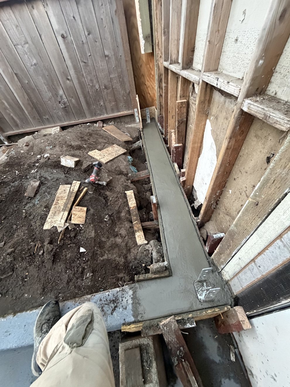 Freshly poured concrete foundation footing beside house framing